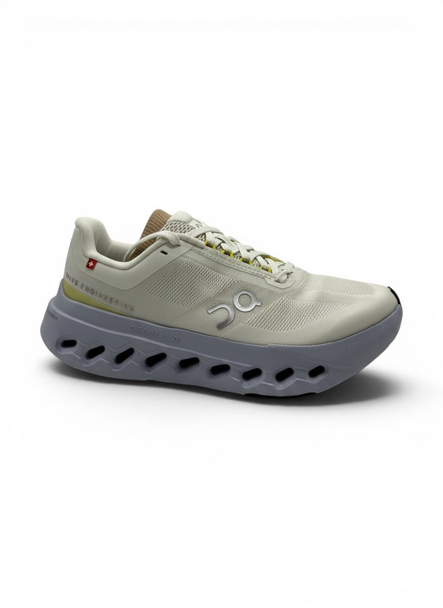 Tenis On Cloud Cloudsurfr Next blancos y grises para mujer, con detalles amarillos y suela de goma. Diseño moderno para uso deportivo y diario.